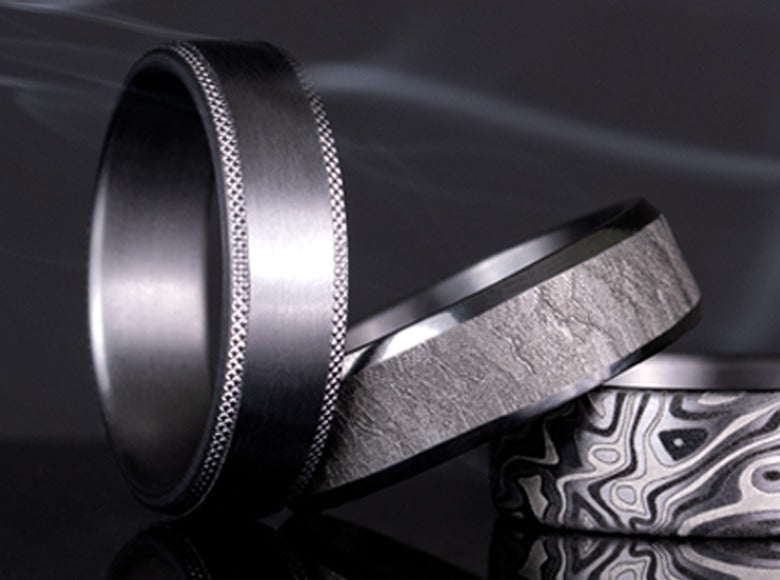 Three tantalum men's wedding bands with brushed, hammered, and mokume finishes at Farsi Jewelers
