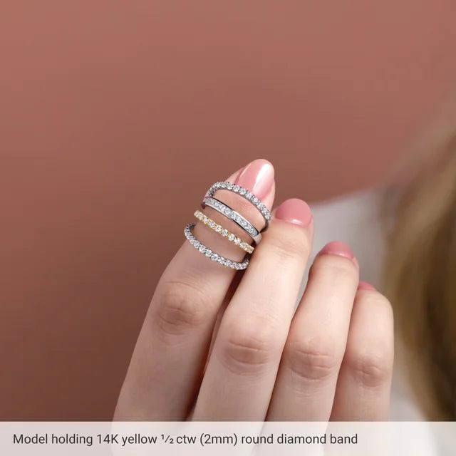 Model holding three slim diamond bands between her fingers, two in white gold and one in yellow; the photo carries a printed caption reading Model holding 14K yellow half ctw 2mm round diamond band
