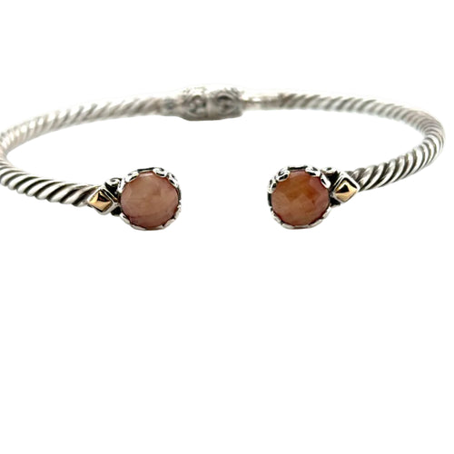 Load image 1 in gallery view. Sterling silver twisted cable bangle photographed in our own showroom, hinged and open at the front, with a round faceted ruby held in a scalloped silver crown at each end and a small 18K gold pyramid beside it. The rubies read pink-toned and opaque rather than transparent red, which is how they look in person.