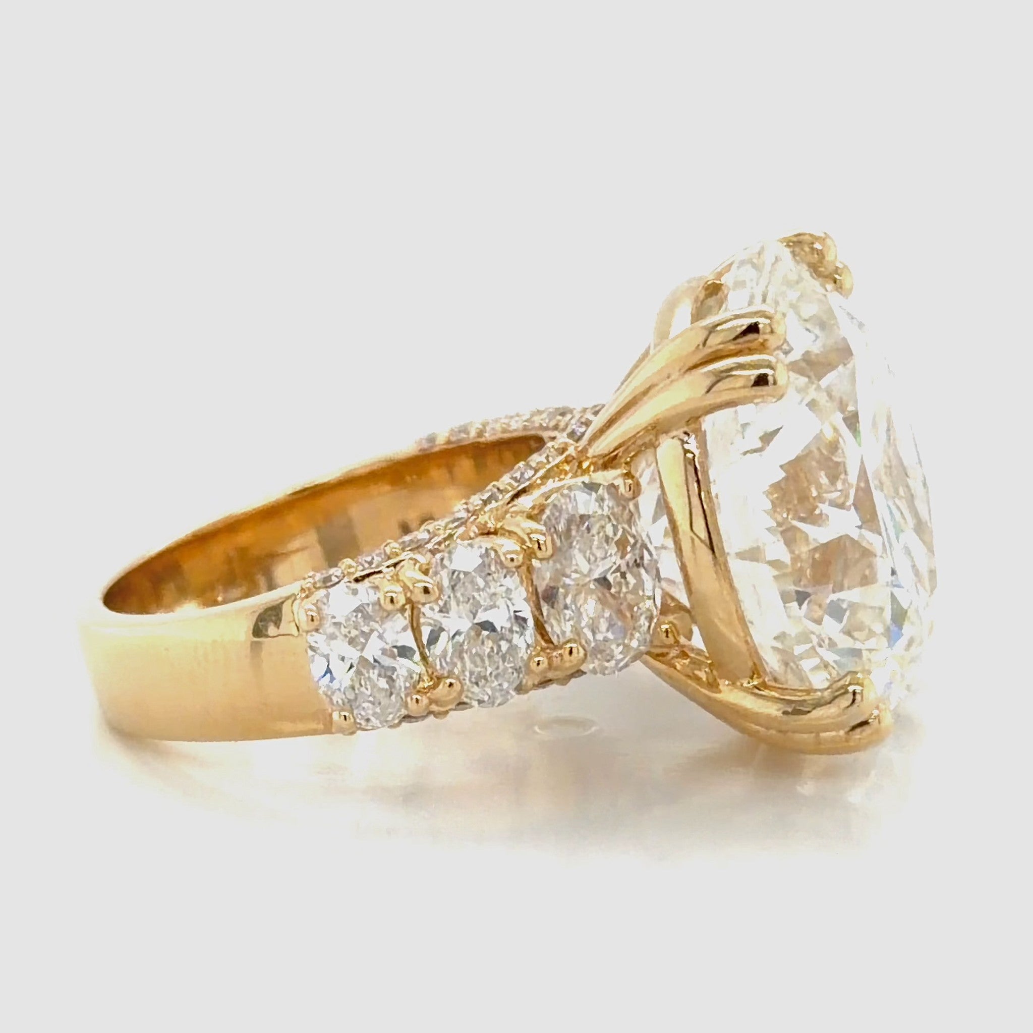 Side profile of a round brilliant diamond engagement ring in 14K yellow gold, three graduated oval diamonds along the shoulder above a pave-set gallery.