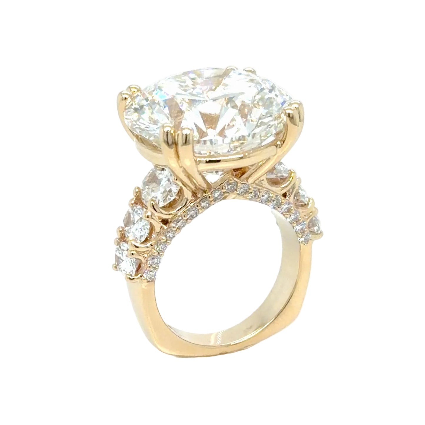 The 24.01 carat round lab-grown diamond at a three-quarter angle, held in paired yellow gold prongs above graduated oval side diamonds and a pave-set band