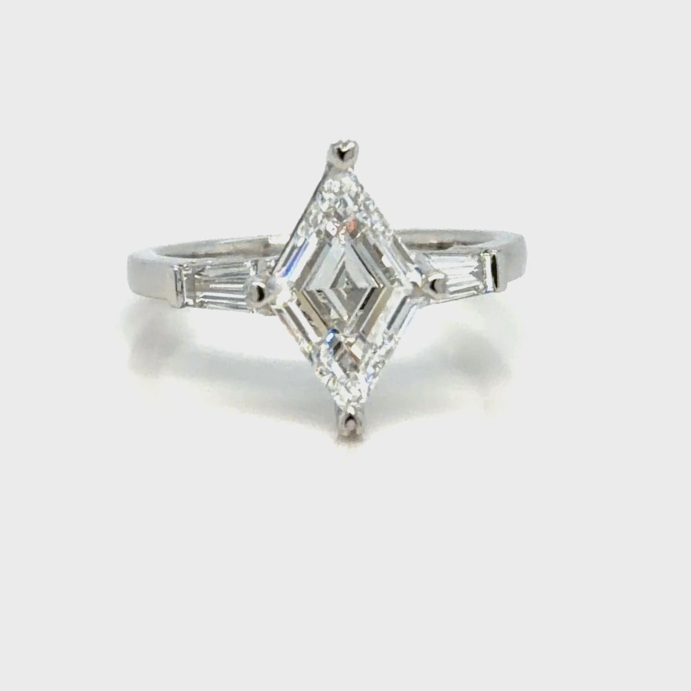 The finished platinum three-stone ring seen face-up, the lozenge-cut diamond set point to point in a prong at each tip, with a tapered baguette diamond angled in on either shoulder