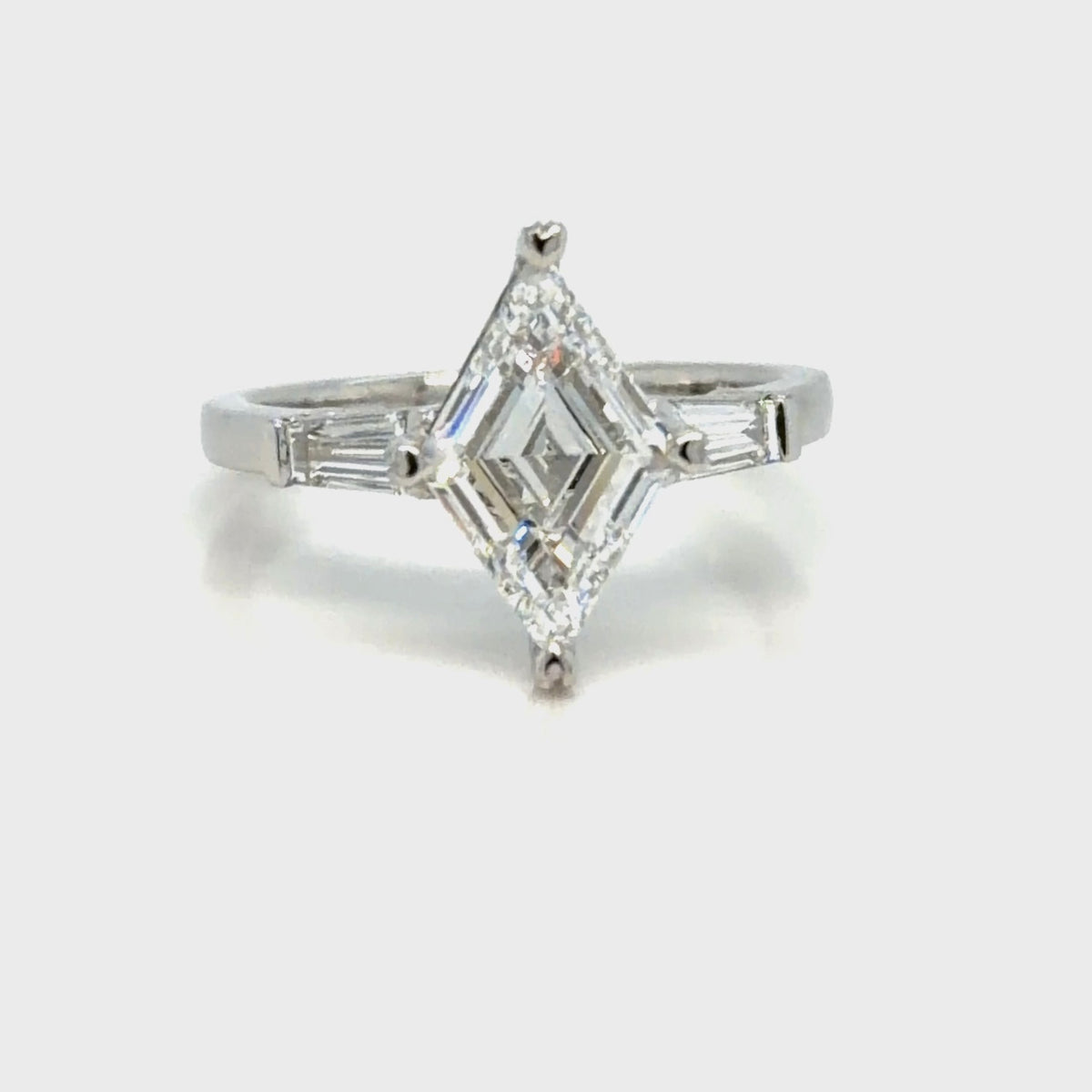 The finished platinum three-stone ring seen face-up, the lozenge-cut diamond set point to point in a prong at each tip, with a tapered baguette diamond angled in on either shoulder