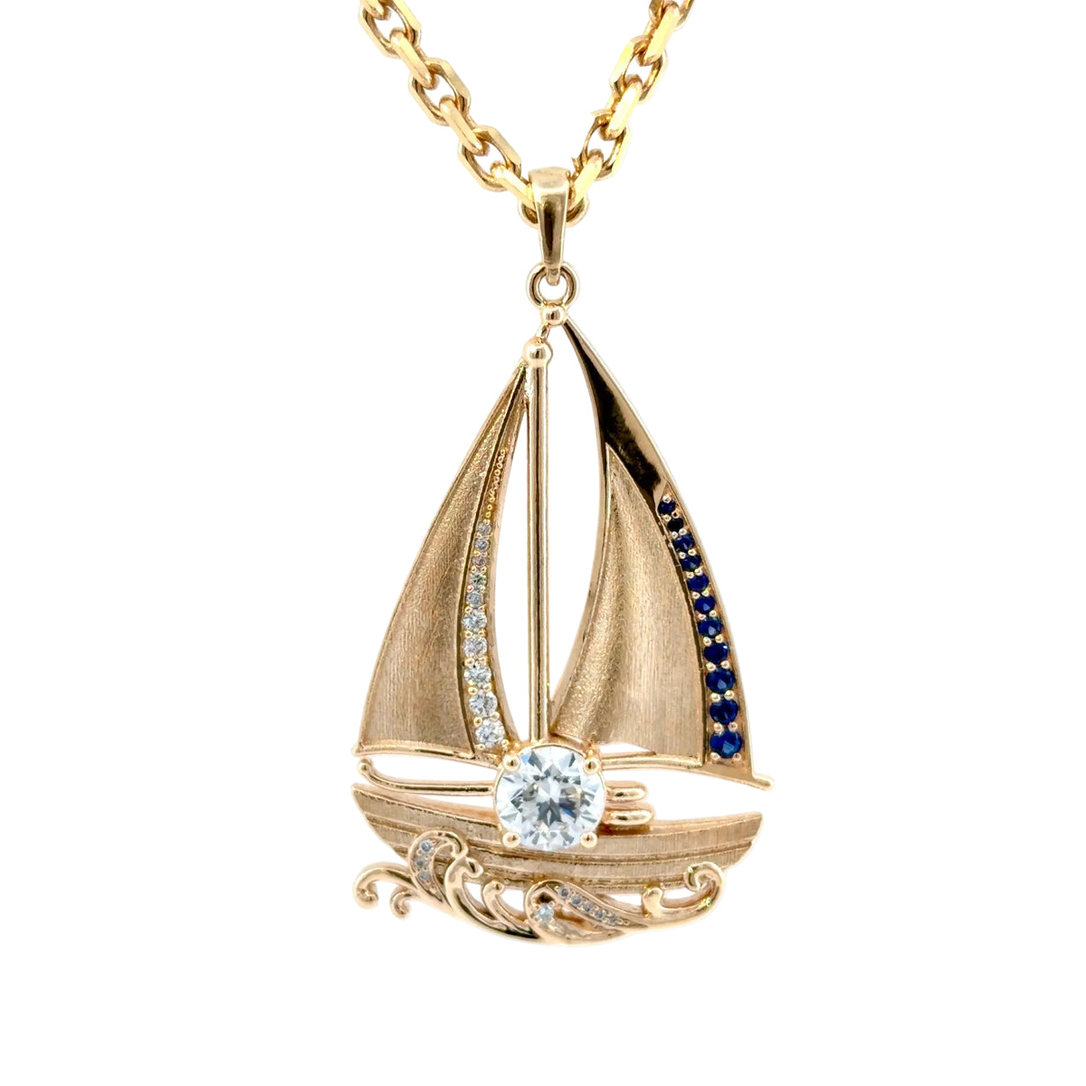 Finished 14K yellow gold sailboat pendant with a round lab-grown diamond at the hull, blue sapphires along one sail and diamonds along the other, on a cable chain, Farsi Jewelers