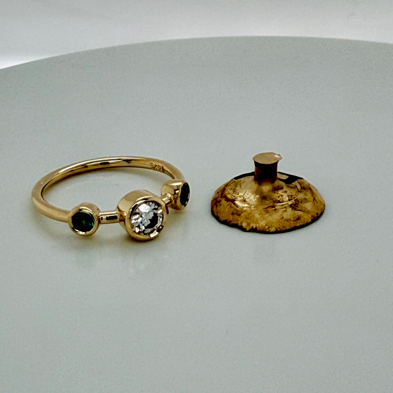 The finished three-stone ring beside the leftover casting button of the customer's own gold, the raw metal that remained after the ring was made and went back to its owner