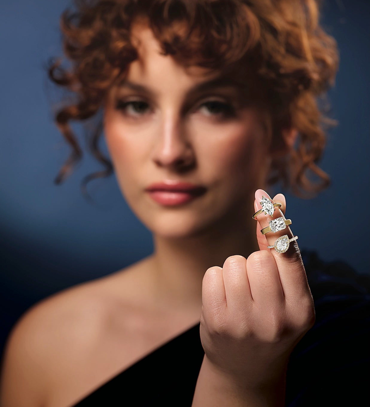 Woman holding three diamond rings on a dark background