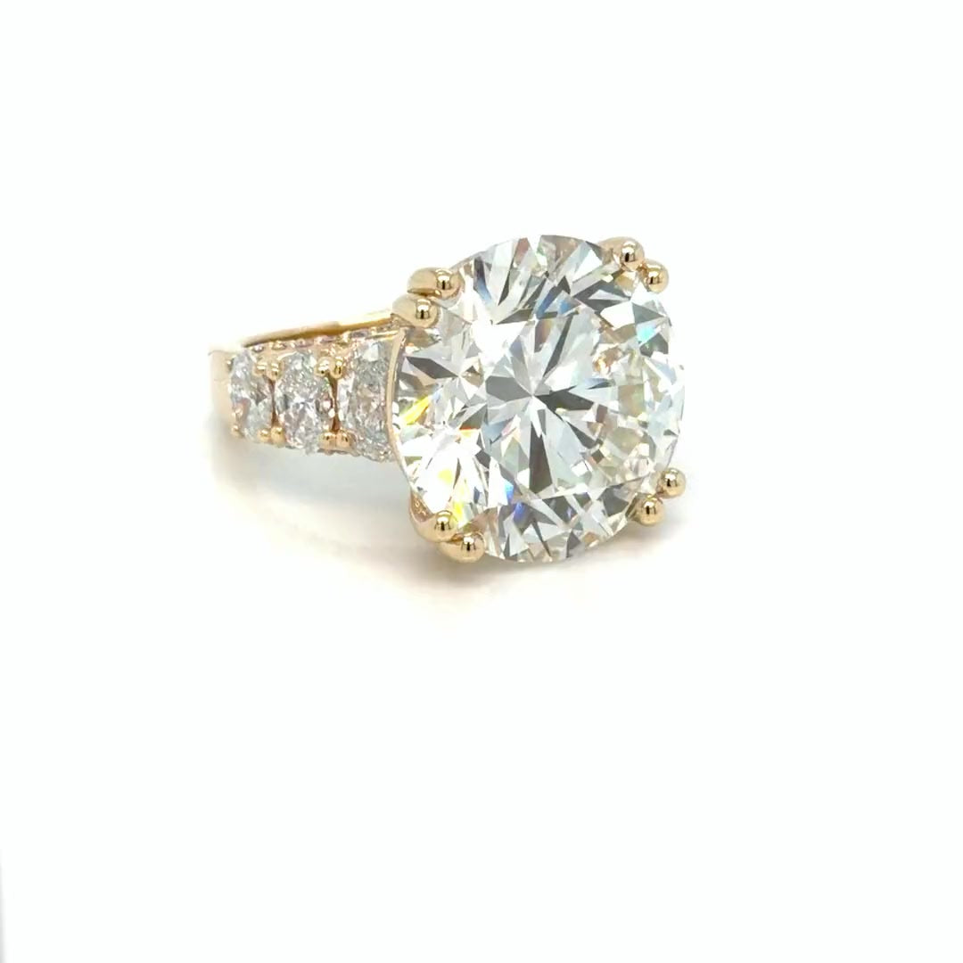The 24.01 carat round lab-grown diamond seen from the side, held in doubled yellow gold prongs above three graduated oval diamonds running down the pave-set shoulder