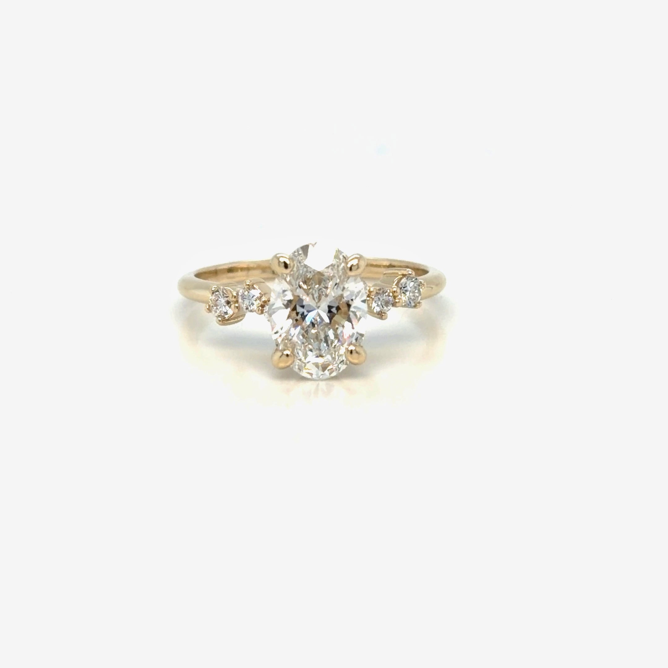 Oval lab-grown diamond engagement ring in 14K yellow gold seen from above, with graduated round diamonds set along asymmetrical shoulders