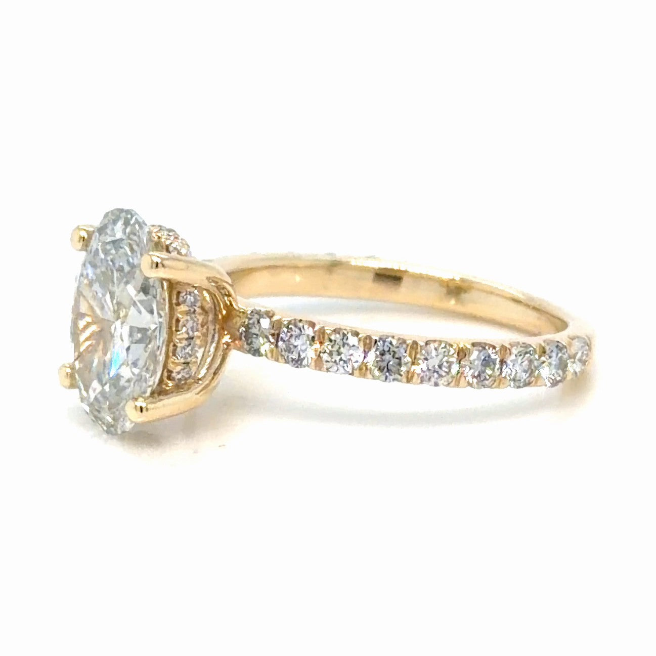 Side view of a 14K yellow gold oval lab-grown diamond engagement ring, showing the hidden halo of small round diamonds set around the head beneath the center stone, and the French set accent diamonds running down the shoulder of the band