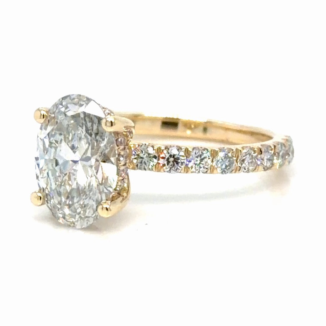 14K yellow gold engagement ring with an oval lab-grown diamond held in four prongs, a hidden halo tucked beneath the center stone, and French set round diamonds along the band
