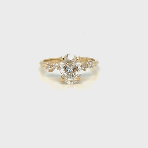 Load image 1 in gallery view. The 14K yellow gold oval lab-grown diamond engagement ring turning slowly, showing the asymmetrical shoulder diamonds and the open setting beneath the center stone