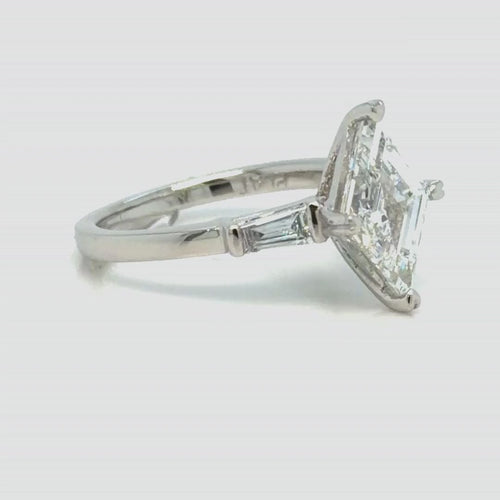 Load image 1 in gallery view. The platinum ring turning slowly from profile toward face-up, showing the lozenge-cut center held at its two points, the tapered baguettes set into the shoulders and the plain platinum band