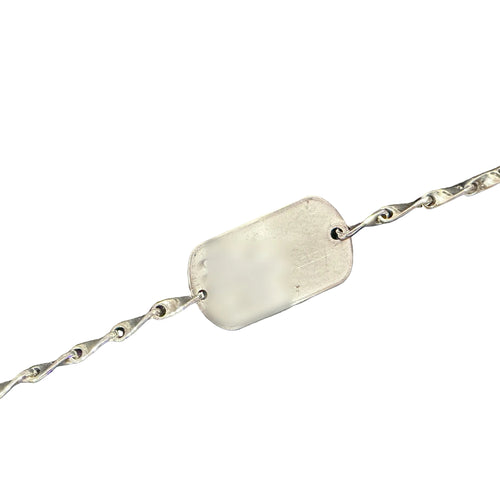 Load image 1 in gallery view. Close view of the dog tag bracelet, showing the twisted sterling links joining each end of the tag and the worn surface of the original tag